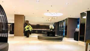 Eine moderne Lobby mit einer zentralen Sitzecke, einem Empfangsbereich und einer großen Pflanze in einem Topf.