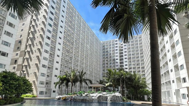 Ein modernes Hochhaus mit einem zentralen Pool, umgeben von Palmen und Liegestühlen.