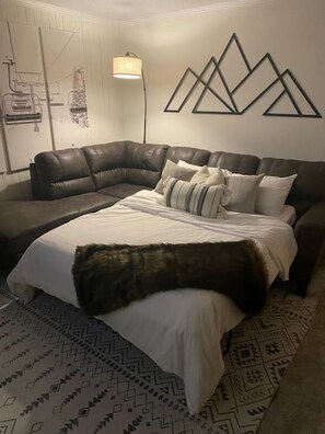 A bedroom with a large bed, a dark leather sofa, a patterned rug, and a wall-mounted light fixture.