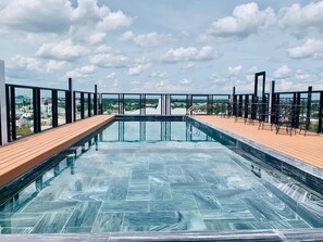 A rooftop infinity pool with a wooden deck, surrounded by metal railings and outdoor seating. - Linh Phuong 6 (Can Tho)