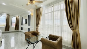 A spacious living room with a ceiling fan, two armchairs, a glass coffee table, and large windows with curtains. - Linh Phuong 6 (Can Tho)