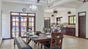Un grand espace à manger avec une longue table dressée pour accueillir plusieurs personnes, un banc et une cuisine en arrière-plan.