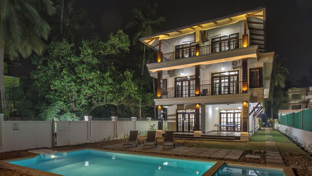 Une maison à deux étages avec une piscine, un espace salon extérieur et un balcon bien éclairé.