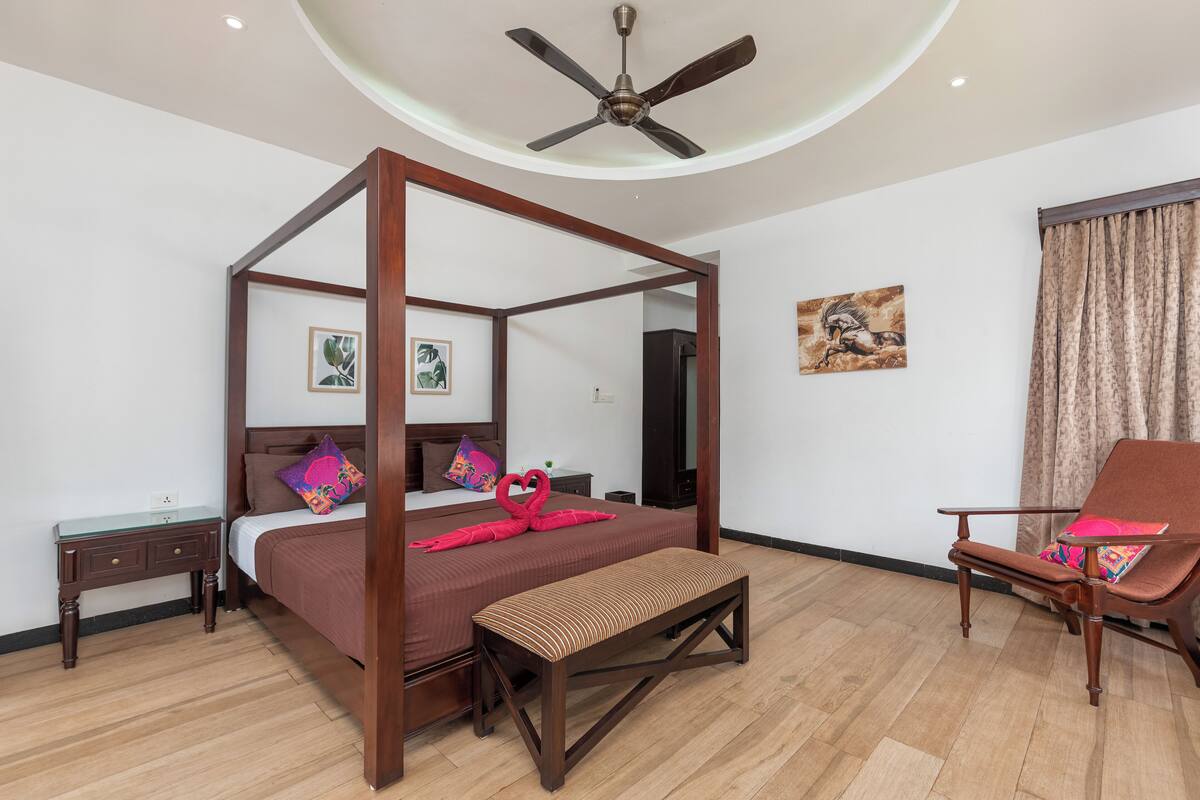 A four-poster bed with a wooden frame, a bench, a chair, and a small table.