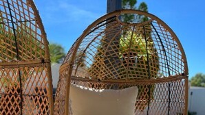 Un área de estar exterior con muebles de mimbre, sillas acolchadas y una mesa trenzada, cada uno con un vaso de jugo de naranja.