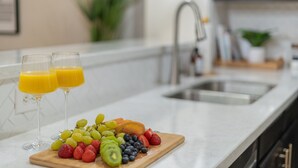 Una encimera de cocina con una bandeja de frutas y dos vasos de jugo de naranja.