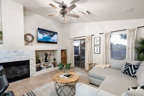 Una sala de estar con chimenea, ventilador de techo, televisor y sofá.