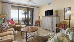 Amplia sala de estar con ventilador de techo, televisor grande, mobiliario de mimbre y vistas al exterior.