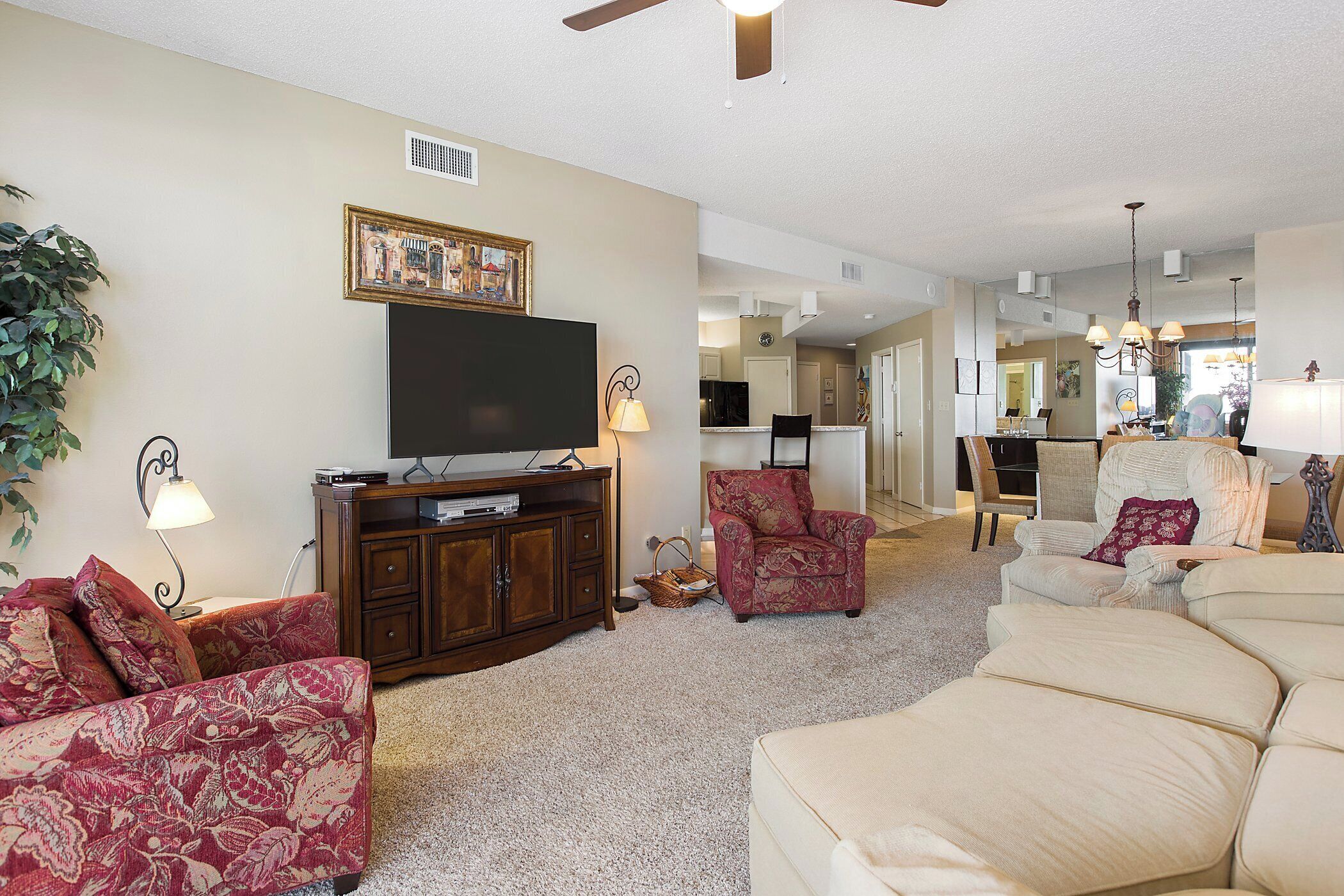 A living room with a flat-screen TV, a red patterned sofa, a beige sofa, and a dining area in the background.
