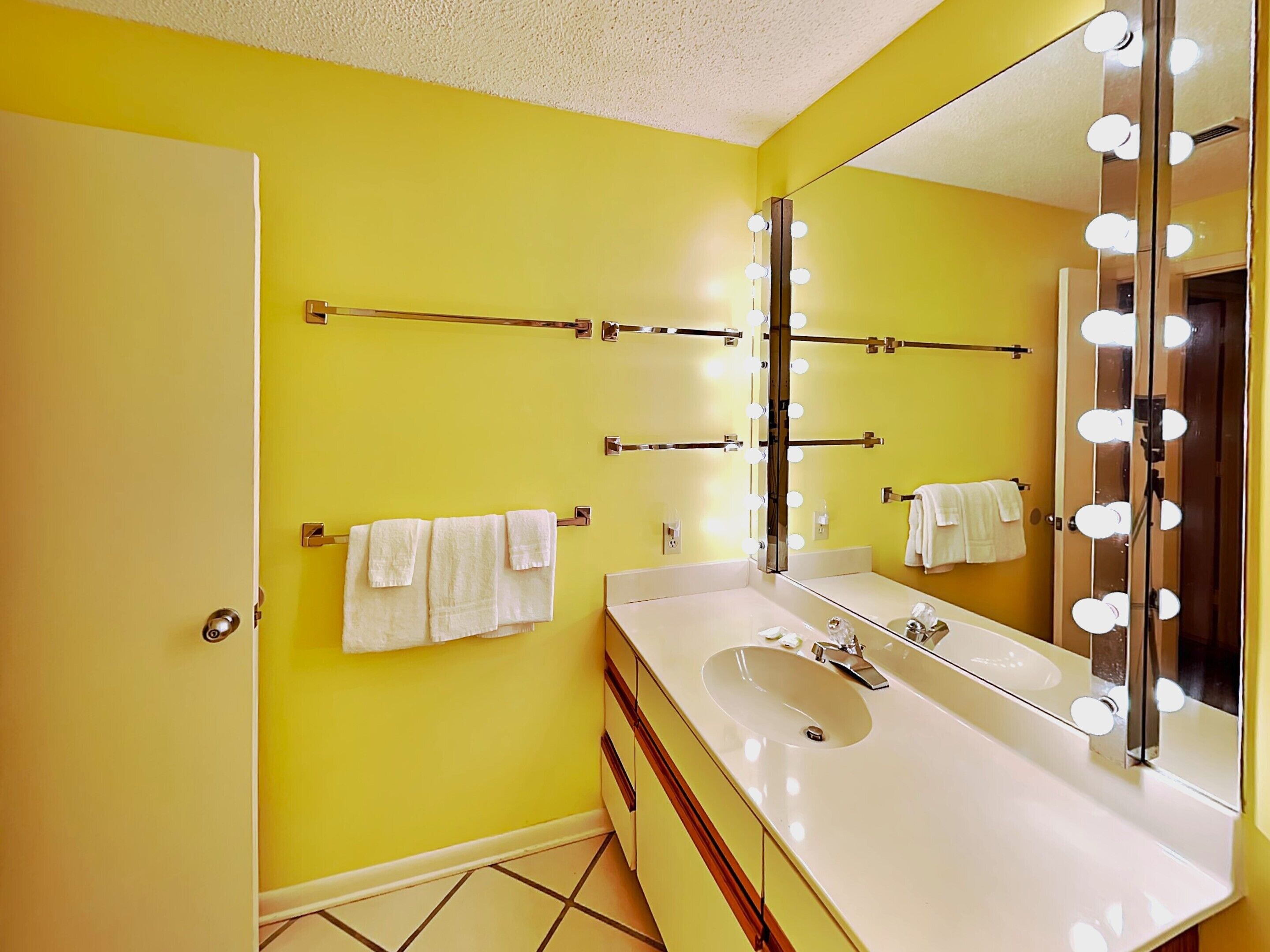 A bathroom with yellow walls, a white sink, and a large mirror with lights.
