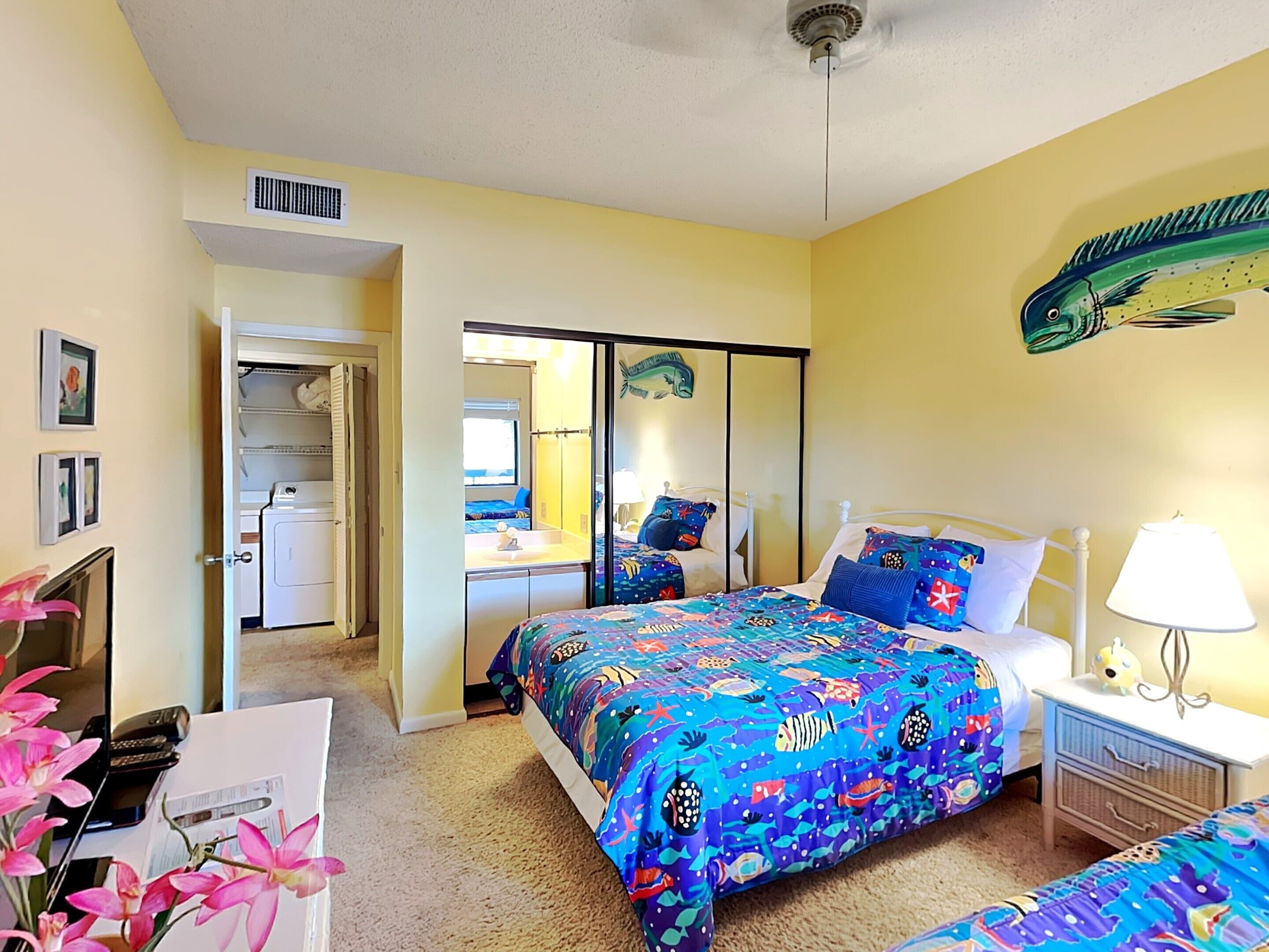 A bedroom with a bed, bedside table, and a desk with a chair. There is a closet with a mirror and a window.