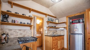 A kitchen with wooden cabinets, a stainless steel refrigerator, a gas stove, and shelves with kitchenware.