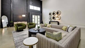 A spacious living area with a large sofa, two armchairs, a coffee table, and a round side table. There are decorative wall mirrors and a large window with a view of the outside. - 3BR Luxury Loft Near Downtown & Frost Bank Center (San Antonio)