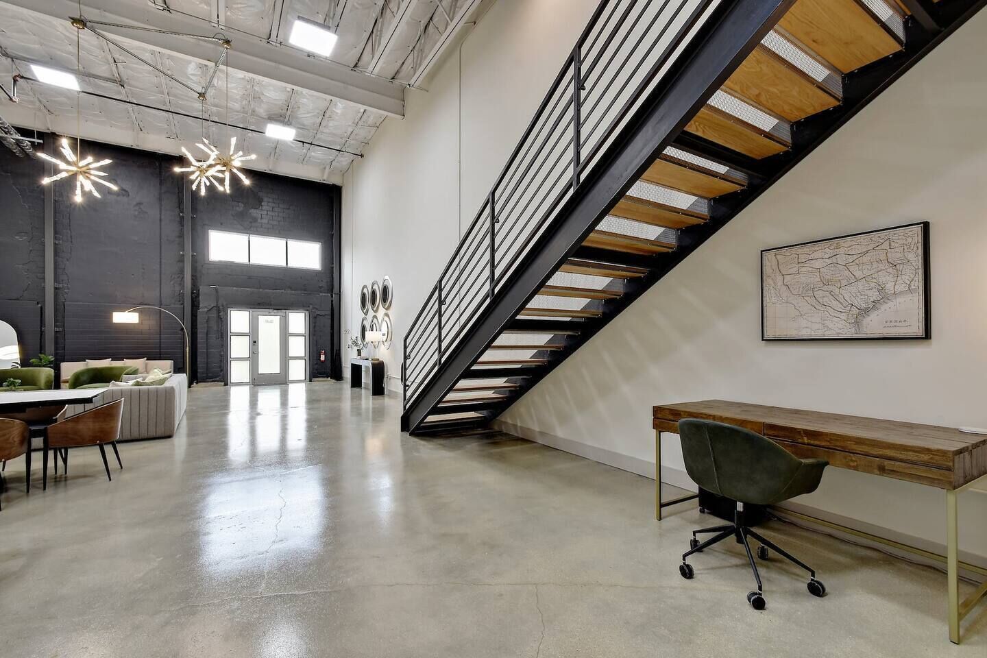 A spacious office with a concrete floor, a wooden desk, and a modern staircase.