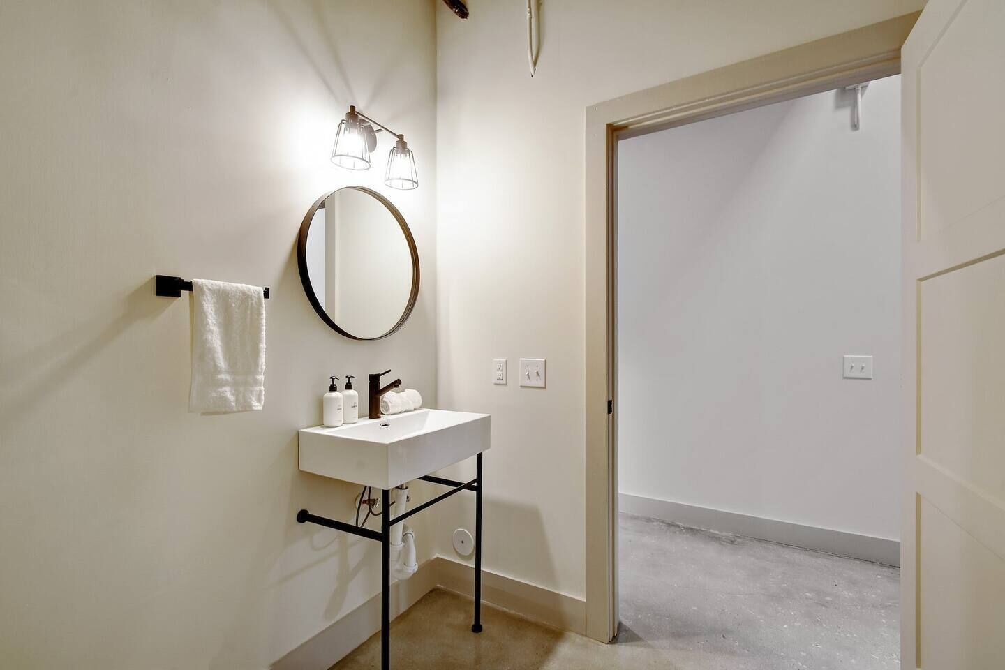 Un baño con un lavamanos blanco, un espejo redondo y dos luces fijadas a la pared.