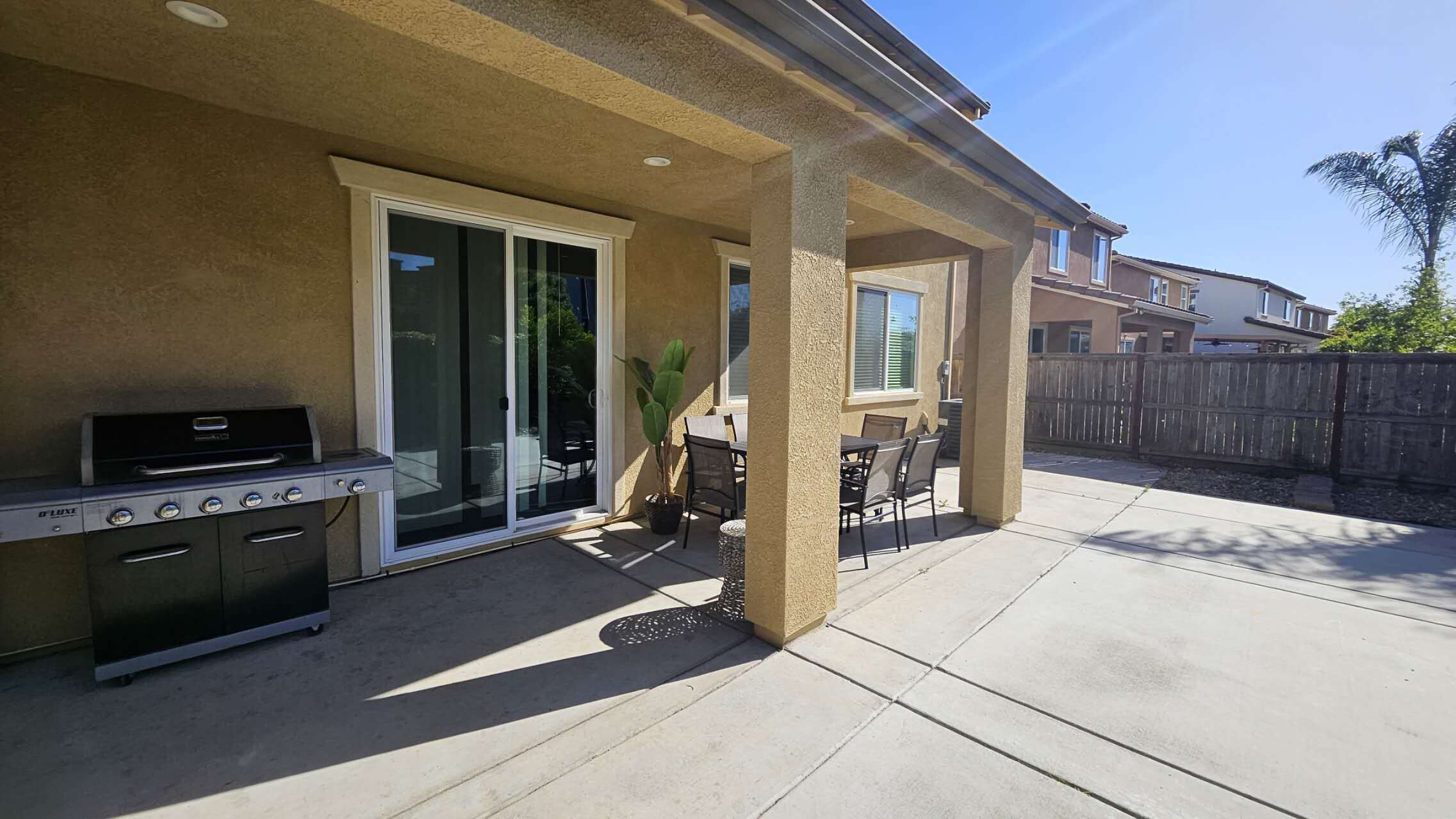 A patio with a grill, sliding glass doors, and a table with chairs.