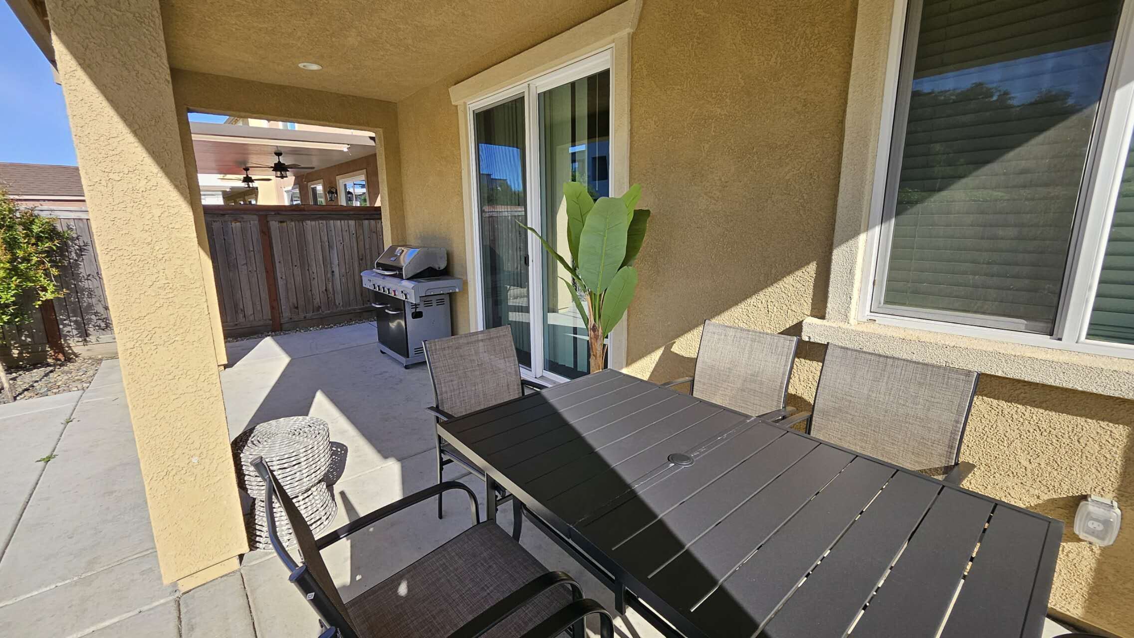 Une terrasse extérieure avec une table et des chaises, un barbecue et une porte-fenêtre coulissante.
