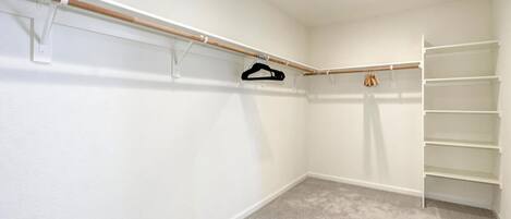 A walk-in closet with a wooden rod, a black hanger, and a white shelving unit.