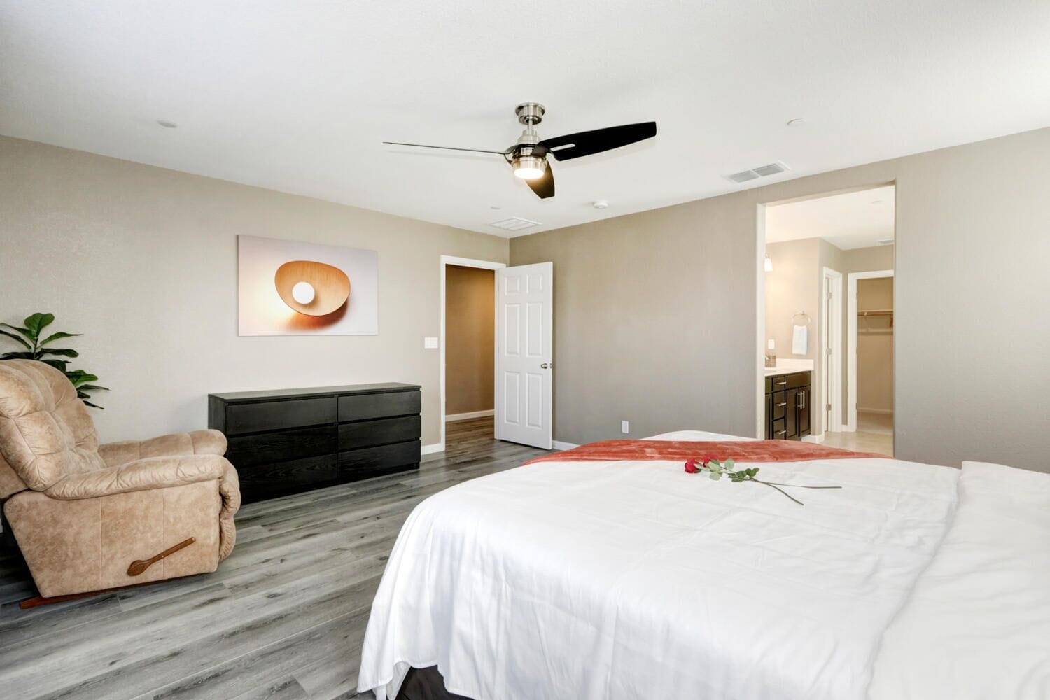 Une chambre à coucher comprenant un lit, une chaise, une commode et un ventilateur de plafond.