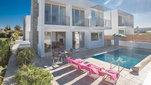 Et moderne hus med to etager, swimmingpool, udendørs siddepladser og en velplejet have.