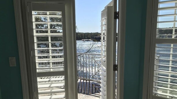 Udsigt gennem en dør med hvide skodder, der fører til en balkon med gelænder og et snelandskab.
