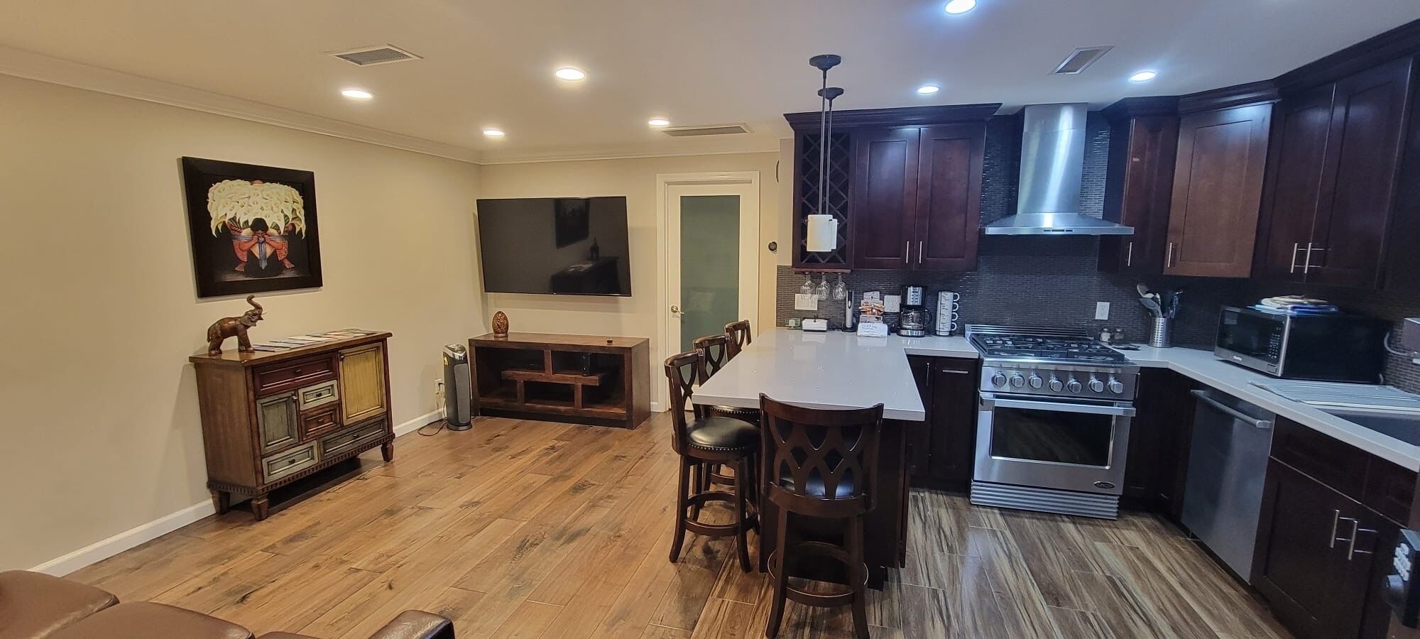 Una cocina moderna con armarios de madera oscura, una estufa de acero inoxidable y un comedor con mesa y sillas de madera.