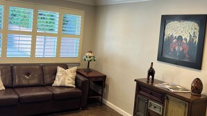Un salon avec un canapé en cuir marron, une petite table avec une lampe, un meuble avec des tiroirs et un tableau encadré accroché au mur.
