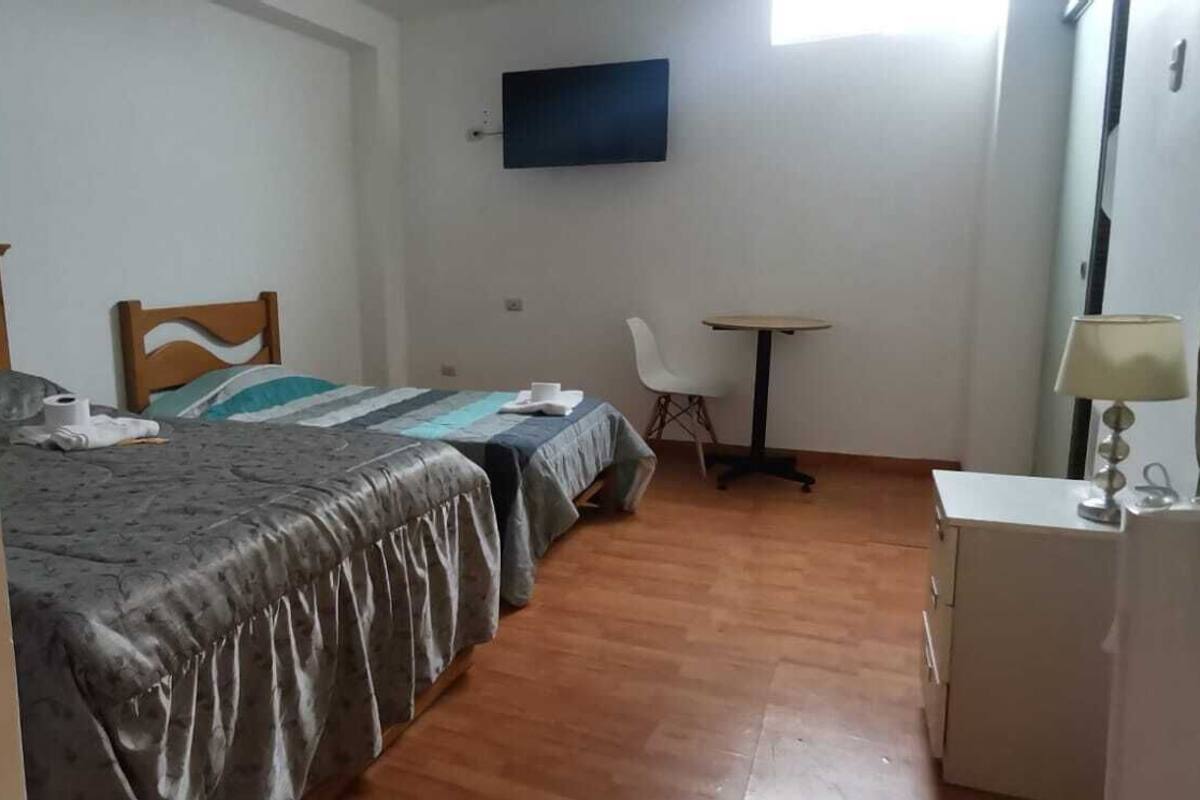A hotel room with two beds, a desk, a chair, a TV, and a lamp.