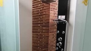 A corner shower stall with a brick-patterned wall, a glass door, and a control panel. - hospedaje pueblo viejo (San Luis de Cañete)