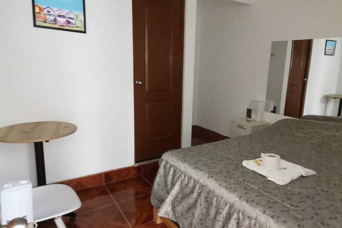 A hotel room with a bed, a small table, a chair, a mirror, and a television.
