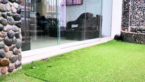 A modern outdoor area with a glass wall, a stone wall, and a well-maintained grassy lawn. - hospedaje pueblo viejo (San Luis de Cañete)