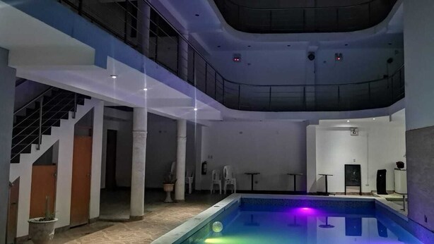 A modern indoor pool area with a glass ceiling, a staircase, and a pool with colorful lighting. - hospedaje pueblo viejo (San Luis de Cañete)