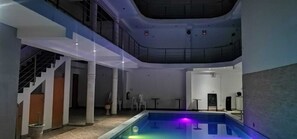 A modern indoor pool area with a glass ceiling, a staircase, and a pool with colorful lighting. - hospedaje pueblo viejo (San Luis de Cañete)