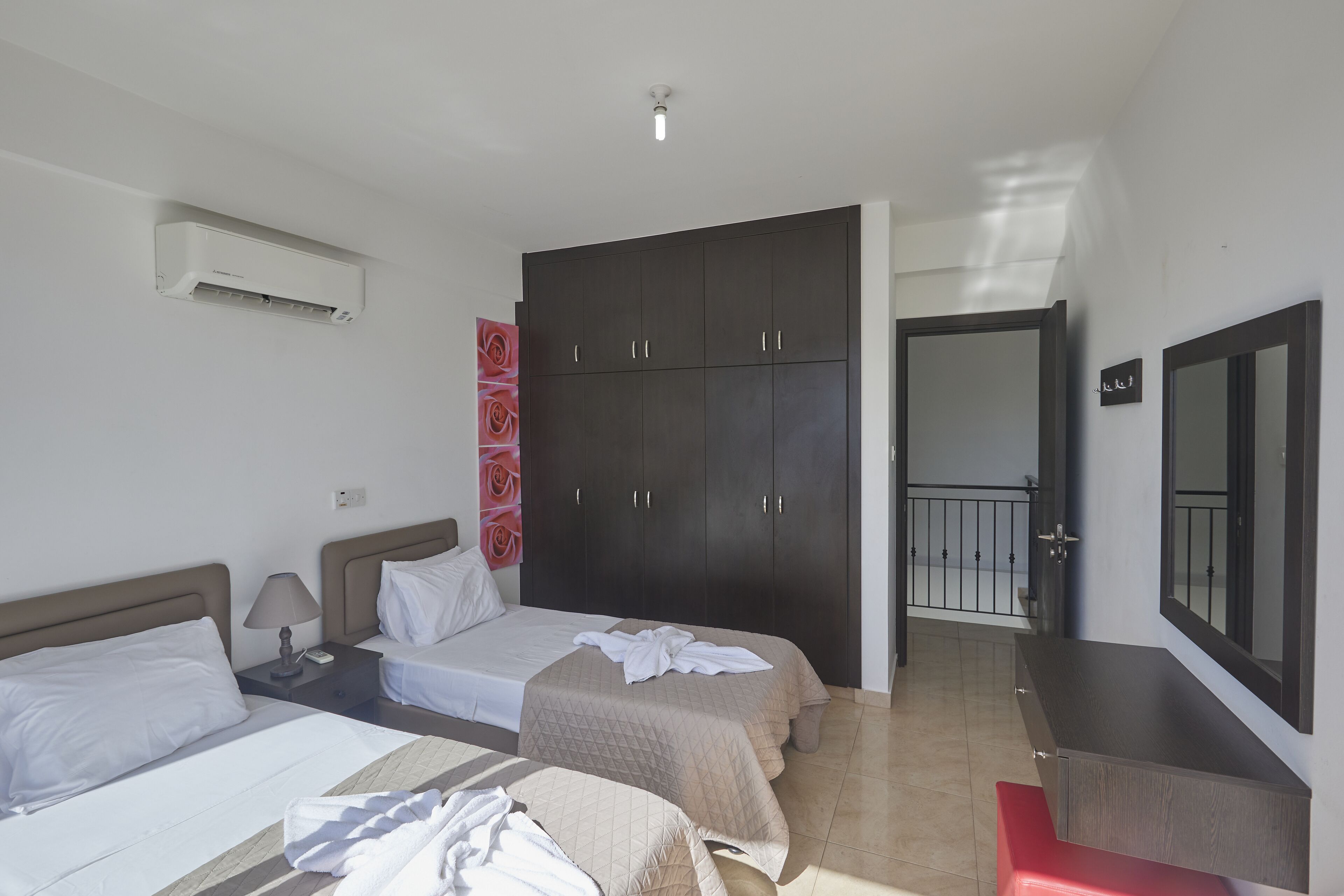 A hotel room with two beds, a wardrobe, a mirror, and an air conditioning unit.