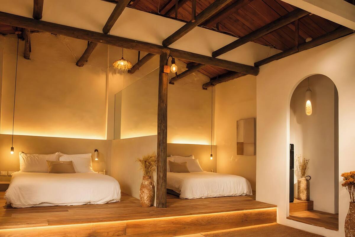 A bedroom with two beds, wooden beams, a vaulted ceiling, and a large mirror.