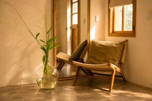Uma cadeira de vime com almofada, um vaso de vidro transparente com uma planta e uma porta de madeira.