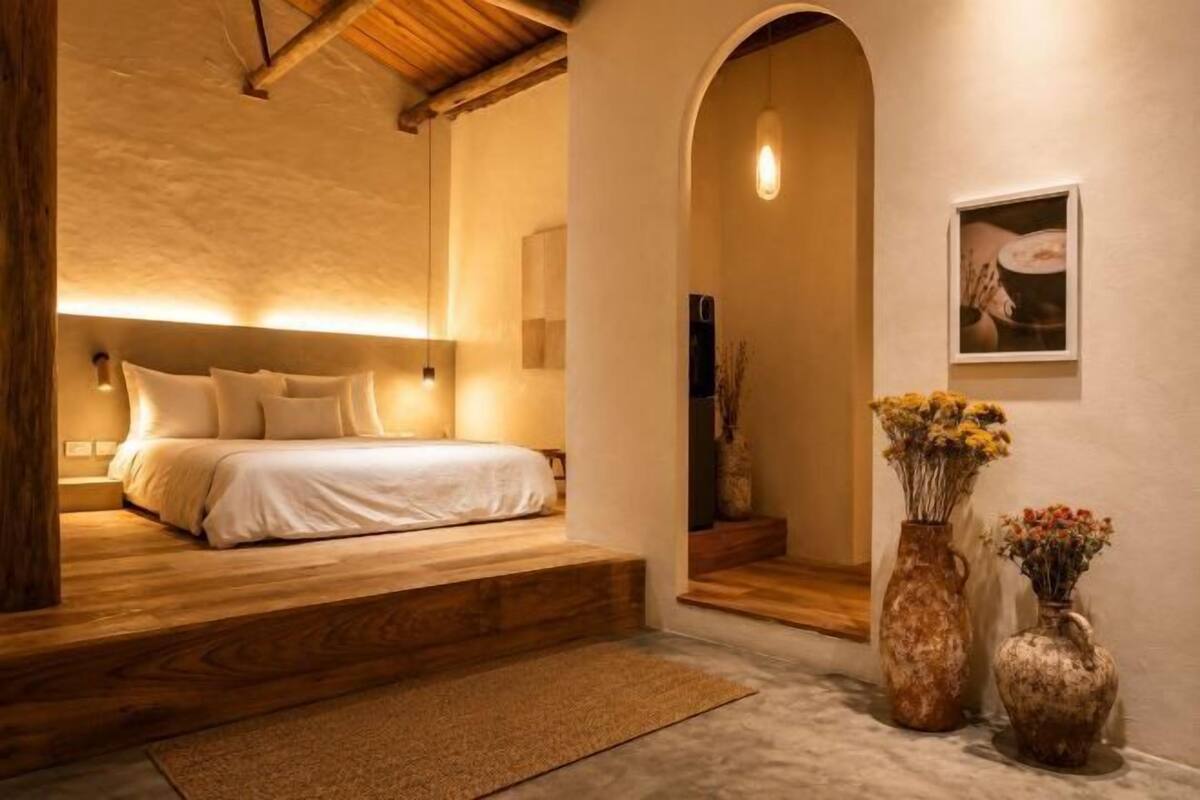 A bedroom with a bed, a wooden staircase, a large arched doorway, and two vases with flowers.