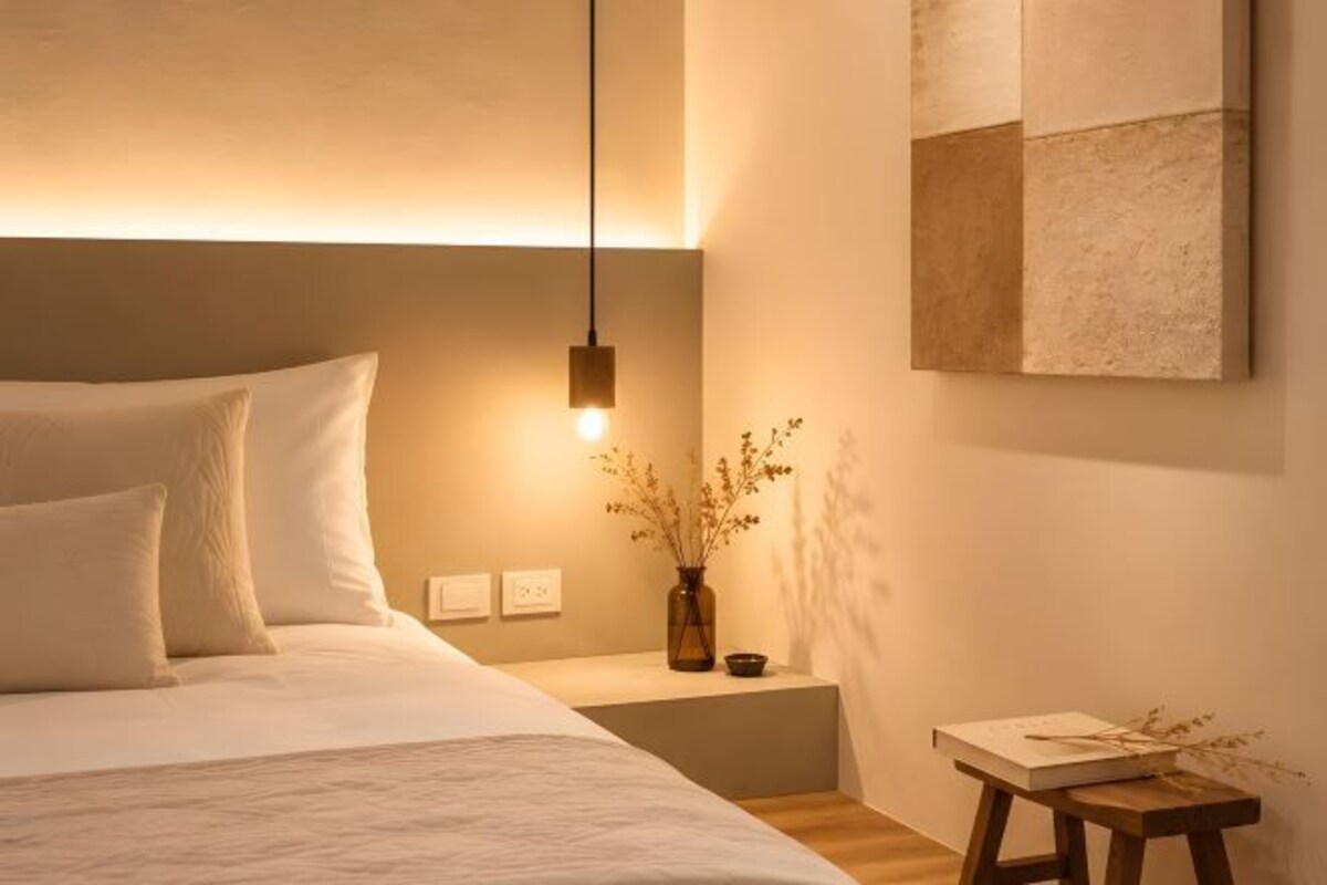 Un dormitorio ordenado con cama, mesita de noche y un taburete pequeño.