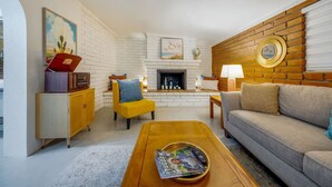 Un salon avec une cheminée, un canapé, un fauteuil jaune et une table basse en bois.