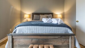 Ein ordentlich gemachtes Bett mit einer gesteppten, blauen Decke, zwei Kissen und einer Nachttischlampe.