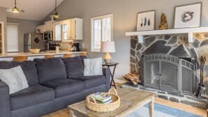 Ein Wohnzimmer mit einer dunkelgrauen Couch, einem Holztisch und einem Kamin aus Stein.