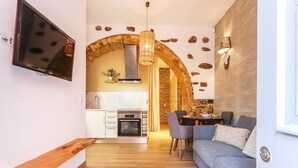 Uma sala de estar moderna com televisão embutida, um banco de madeira, um sofá cinzento e um espaço de jantar com mesa e cadeiras.