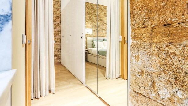 Quarto de hotel moderno com parede de tijolos, piso de madeira e cama em esquema de cores verde e branco.