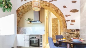 Cozinha moderna com armários brancos, forno embutido e área de jantar com parede de pedra ao fundo.