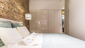 Quarto moderno com parede de tijolos, cama com roupa de cama branca, luminária pendente e guarda-roupa.