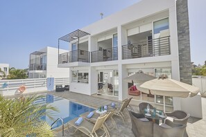 A modern multi-story building with a rooftop pool, outdoor seating, and a covered patio area.