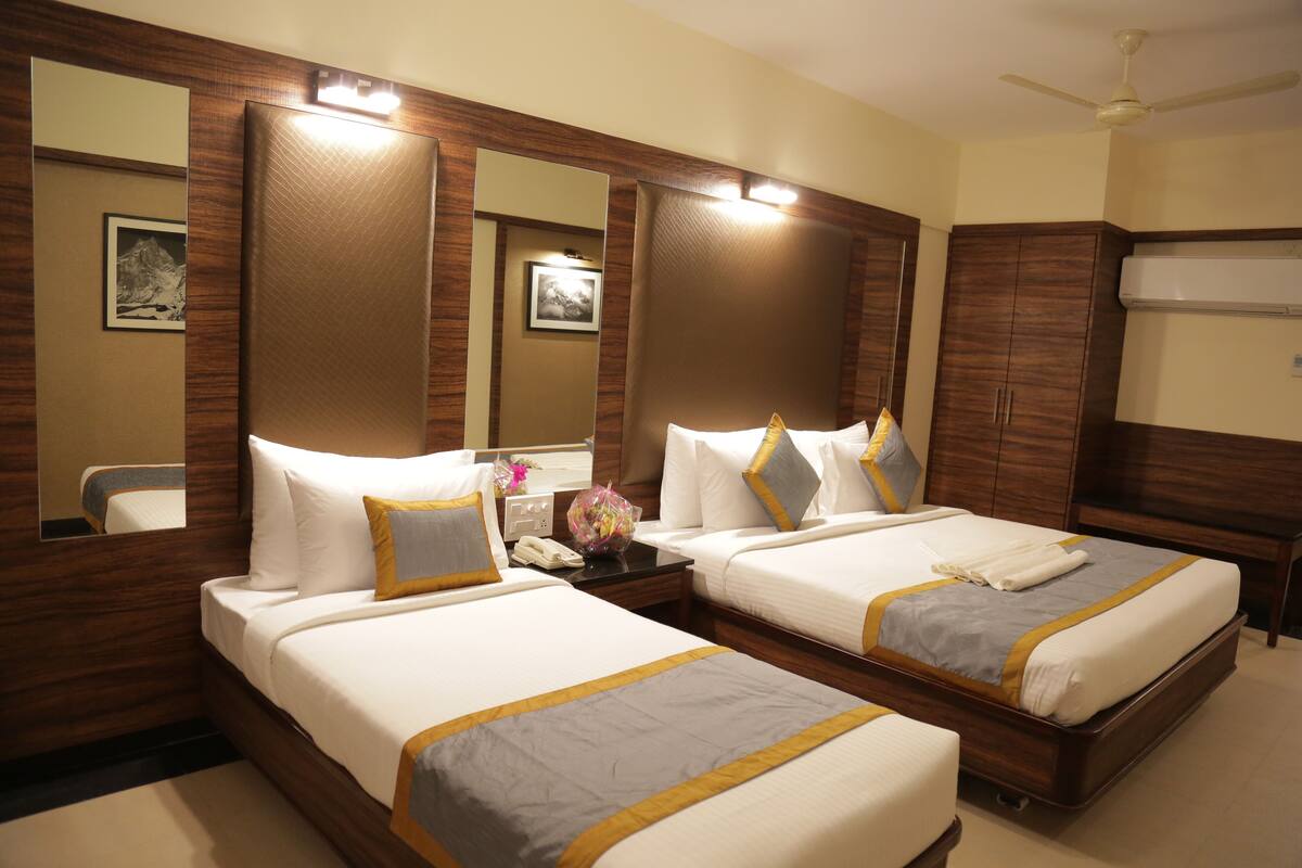 A hotel room with two beds, a mirror, a nightstand, a phone, and a ceiling fan.
