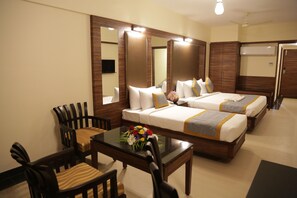 A hotel room with two beds, a dining table, chairs, a mirror, and a TV.