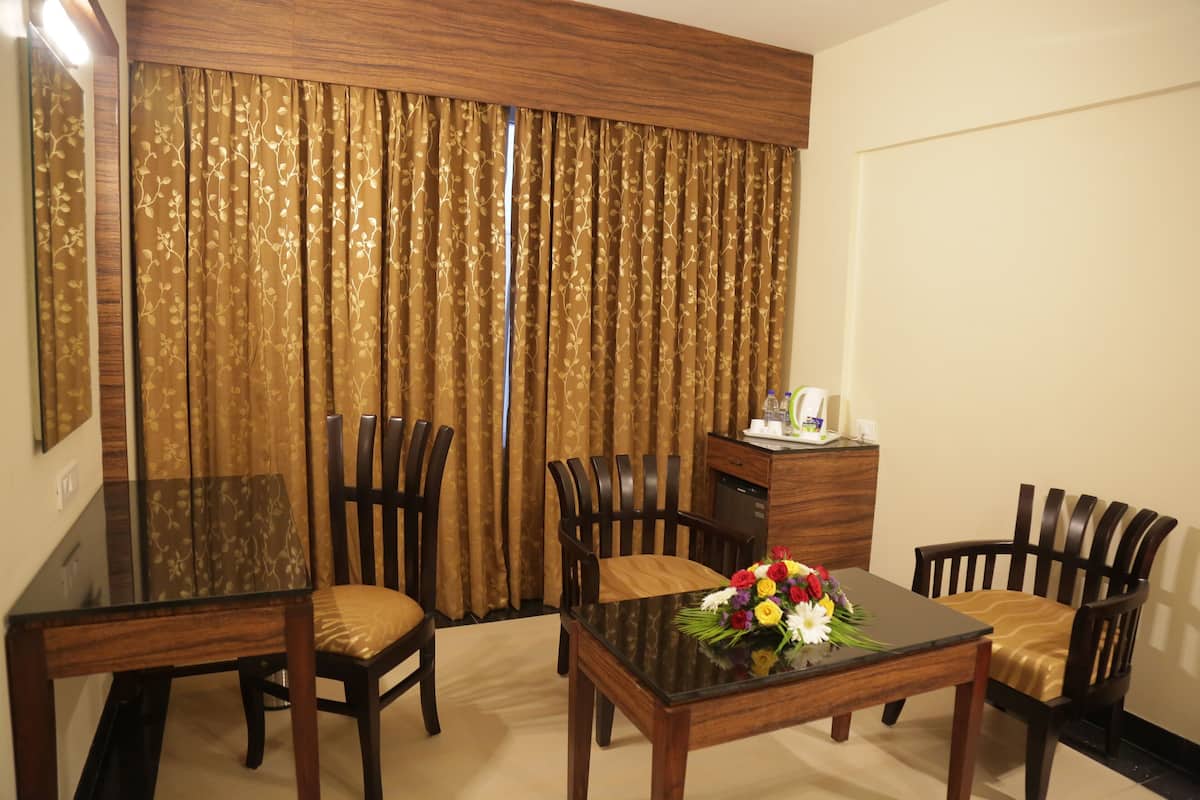 A hotel room with a dining table, four chairs, a small cabinet, and a curtain with a floral pattern.