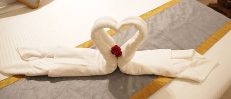 A bed with a heart-shaped towel arrangement and a red rose.